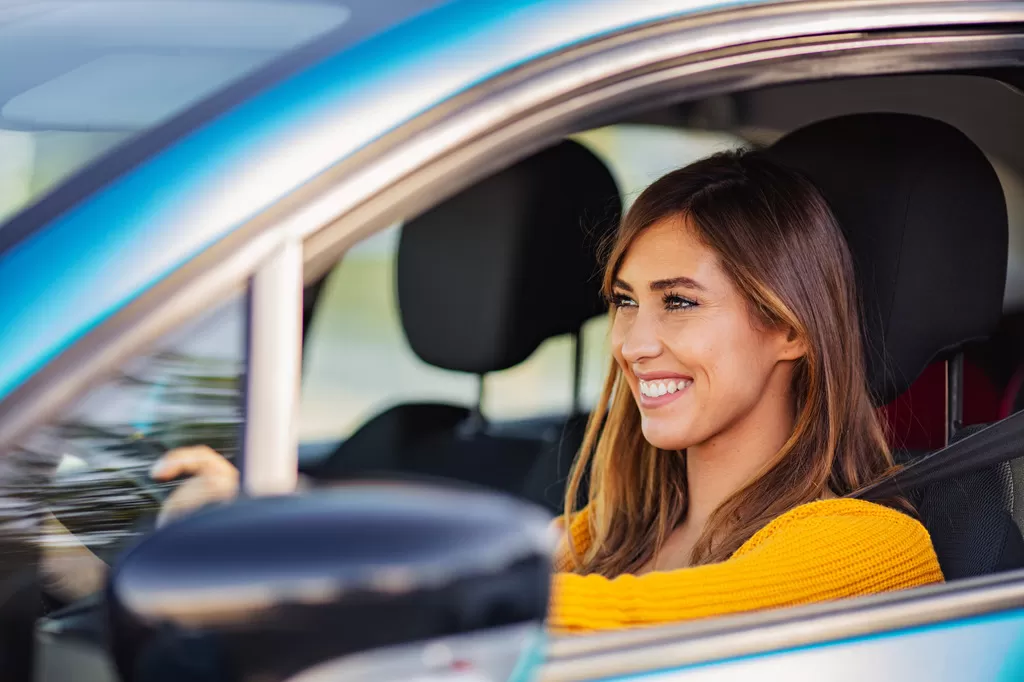 A smiling woman drives away in a car she financed with a credit union auto loan.